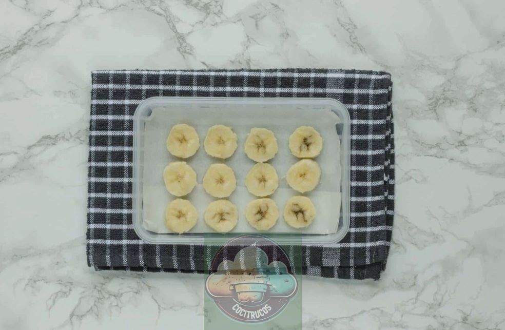 Rodajas de plátano forradas en papel pergamino en un recipiente Tupperware